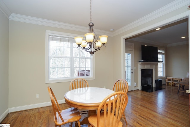 dining room featuring a notable chandelier, a tile fireplace, dark wood-type flooring, and crown molding