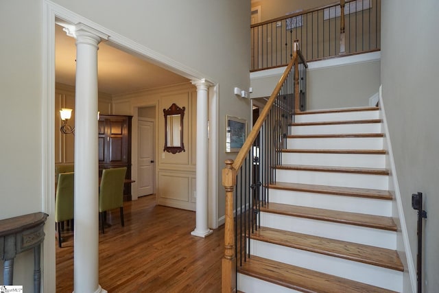 stairway with hardwood / wood-style floors, decorative columns, and ornamental molding