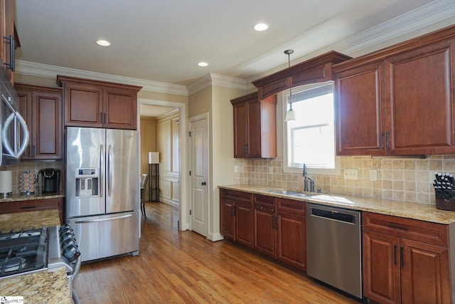 kitchen featuring appliances with stainless steel finishes, pendant lighting, tasteful backsplash, sink, and light hardwood / wood-style flooring