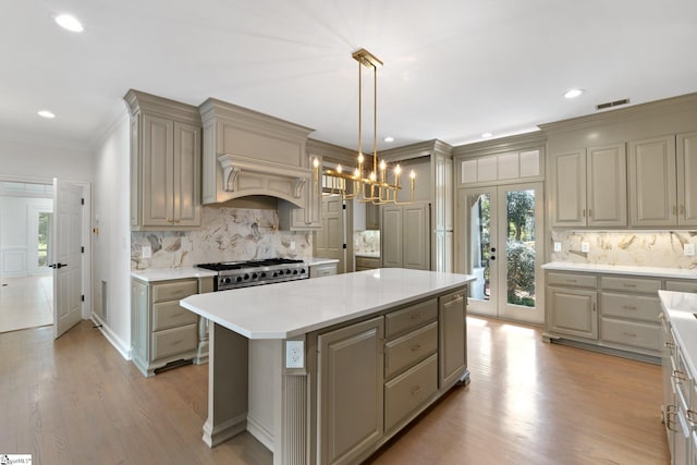 kitchen featuring french doors, a kitchen island, a chandelier, backsplash, and light hardwood / wood-style floors