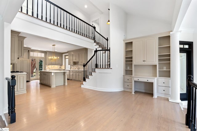 unfurnished living room with light hardwood / wood-style floors, a towering ceiling, a notable chandelier, ornamental molding, and decorative columns