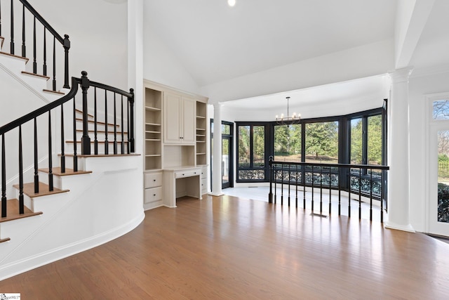 interior space with an inviting chandelier, high vaulted ceiling, ornate columns, and hardwood / wood-style flooring