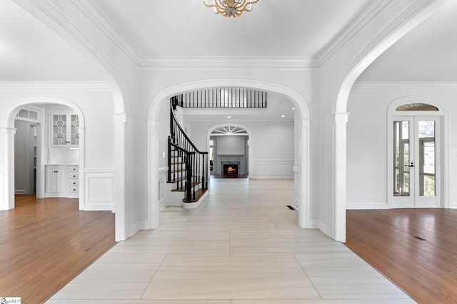 hall with ornamental molding, light tile floors, french doors, and an inviting chandelier