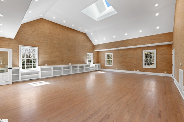 unfurnished living room with high vaulted ceiling, light wood-type flooring, and a skylight