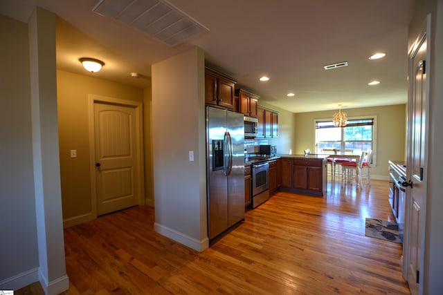 kitchen featuring kitchen peninsula, pendant lighting, an inviting chandelier, hardwood / wood-style flooring, and appliances with stainless steel finishes