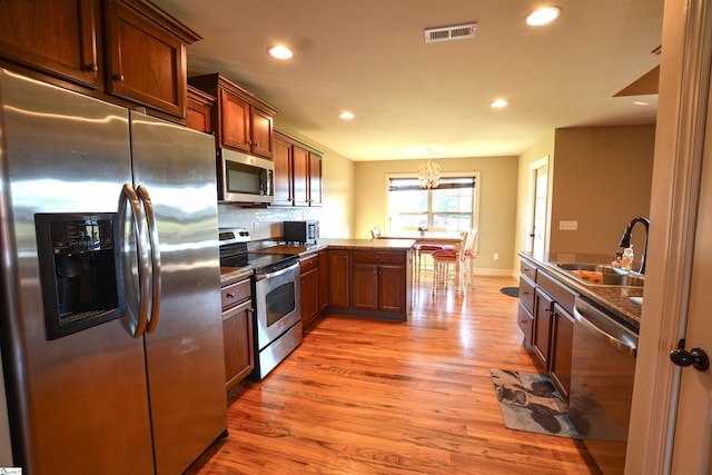 kitchen with kitchen peninsula, hardwood / wood-style floors, tasteful backsplash, stainless steel appliances, and a notable chandelier