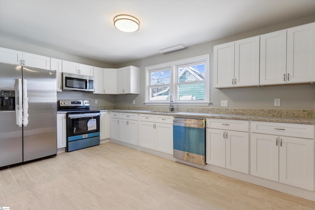 kitchen with light stone countertops, sink, light wood-type flooring, stainless steel appliances, and white cabinets