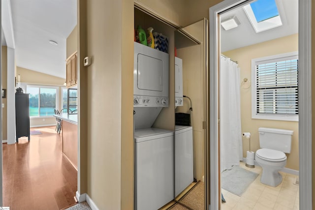 clothes washing area with a skylight, stacked washer / dryer, plenty of natural light, and light wood-type flooring