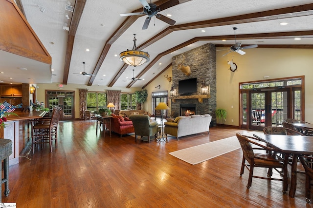 living room featuring dark wood-type flooring, ceiling fan, beamed ceiling, a stone fireplace, and french doors