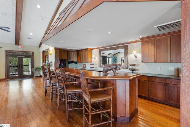 kitchen with light wood-type flooring, a kitchen island, a kitchen breakfast bar, oven, and french doors