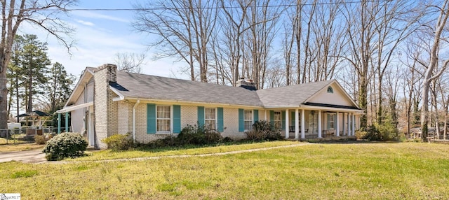 view of front of house with covered porch, brick siding, a chimney, and a front yard