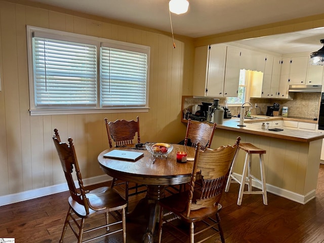 dining space with dark hardwood / wood-style flooring, wooden walls, and sink