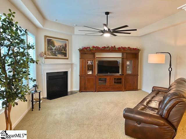 carpeted living room with a tray ceiling and ceiling fan