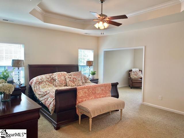 carpeted bedroom with ceiling fan, ornamental molding, and a tray ceiling