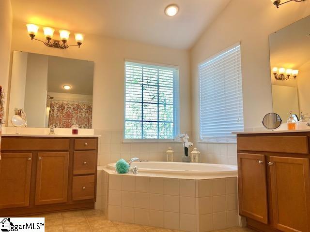 bathroom with lofted ceiling, tile flooring, vanity, and tiled tub