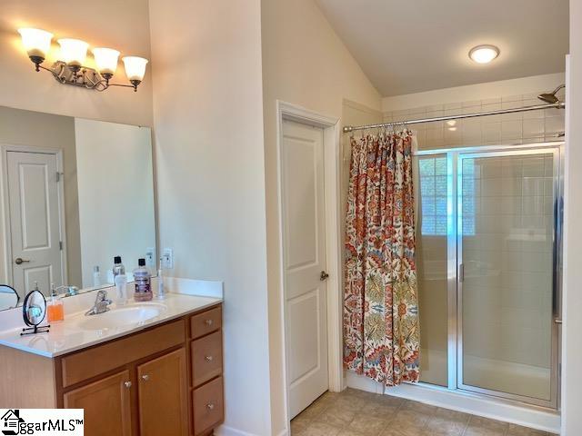 bathroom with tile floors, lofted ceiling, oversized vanity, and walk in shower