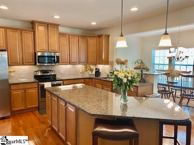 kitchen featuring light hardwood / wood-style floors, stainless steel appliances, decorative light fixtures, a kitchen bar, and a center island