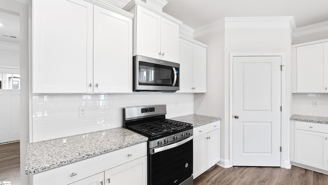 kitchen featuring appliances with stainless steel finishes, white cabinets, ornamental molding, light stone counters, and dark wood-type flooring