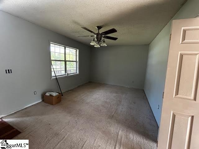 spare room with a textured ceiling, ceiling fan, and dark colored carpet