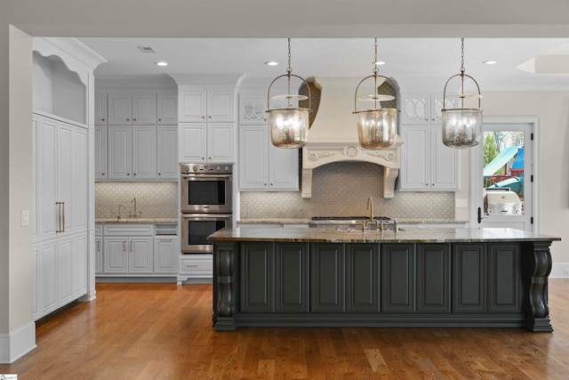 kitchen featuring a kitchen island with sink, backsplash, stainless steel double oven, and light hardwood / wood-style floors