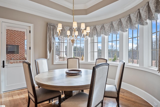 dining space featuring an inviting chandelier, crown molding, a raised ceiling, and light hardwood / wood-style floors