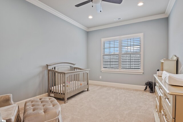 carpeted bedroom featuring ornamental molding, ceiling fan, and a crib