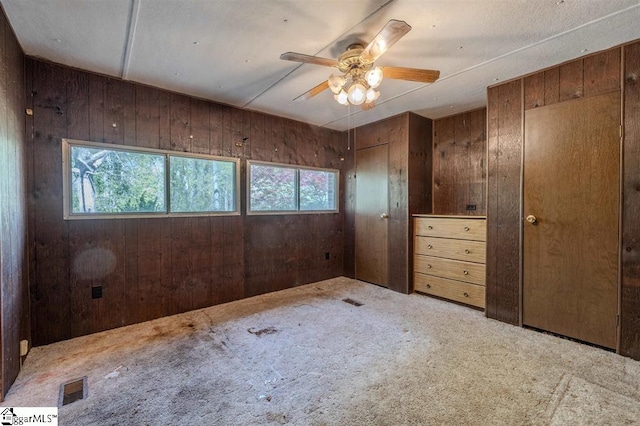 carpeted spare room with wooden walls, a healthy amount of sunlight, and ceiling fan