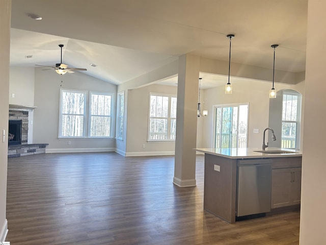 kitchen featuring stainless steel dishwasher, ceiling fan with notable chandelier, a center island with sink, a stone fireplace, and hanging light fixtures