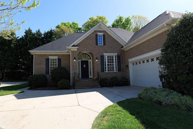 traditional-style house featuring an attached garage, roof with shingles, concrete driveway, and brick siding