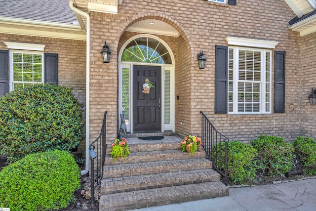 doorway to property featuring brick siding and a shingled roof