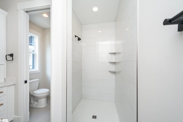 bathroom featuring vanity, toilet, a tile shower, and tile flooring