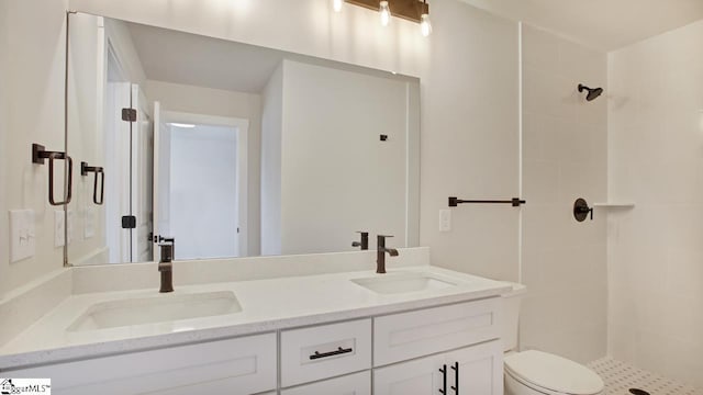 bathroom featuring toilet, dual vanity, and a tile shower