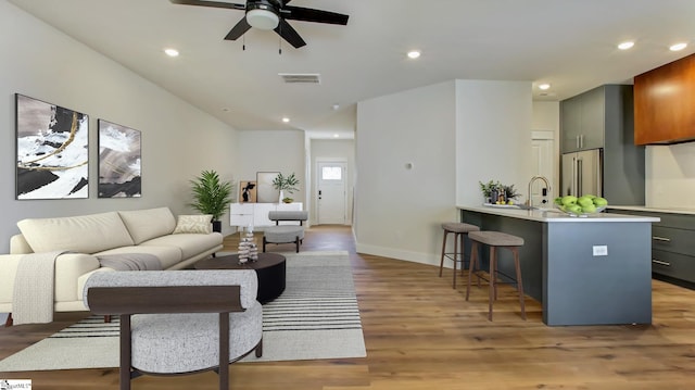 living room with sink, ceiling fan, and light wood-type flooring