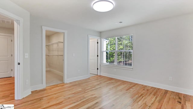 unfurnished bedroom with a closet, a walk in closet, and light wood-type flooring