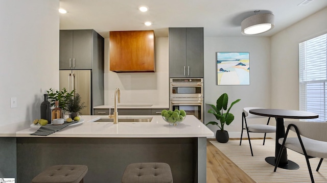 kitchen featuring a kitchen bar, sink, gray cabinets, stainless steel double oven, and light hardwood / wood-style flooring