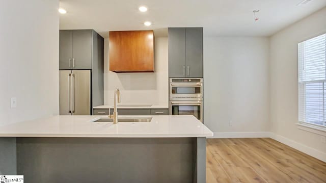 kitchen with sink, light wood-type flooring, double oven, and gray cabinets