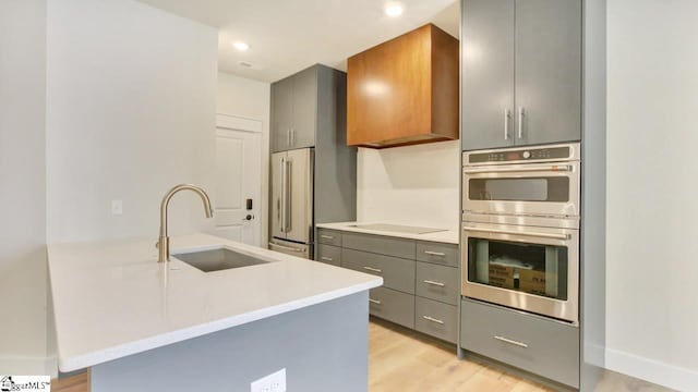 kitchen featuring light stone counters, appliances with stainless steel finishes, sink, light wood-type flooring, and gray cabinetry