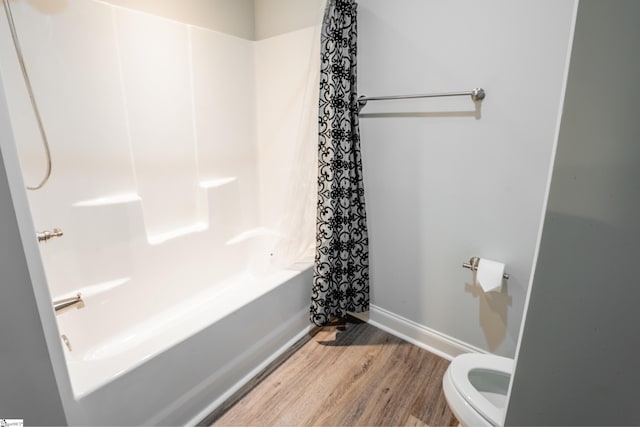 bathroom with washtub / shower combination, hardwood / wood-style flooring, and toilet