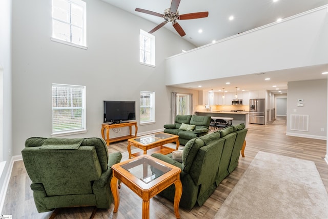 living room with a healthy amount of sunlight, ceiling fan, a towering ceiling, and light hardwood / wood-style floors