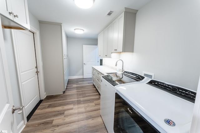 kitchen featuring white cabinets, sink, light hardwood / wood-style flooring, and washing machine and clothes dryer