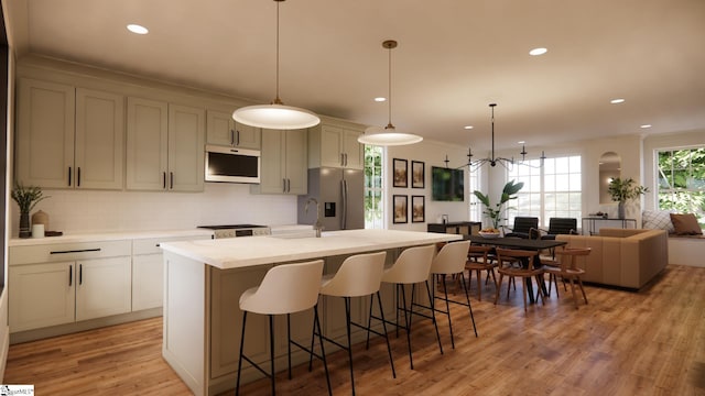 kitchen with a breakfast bar, pendant lighting, light wood-type flooring, and an island with sink