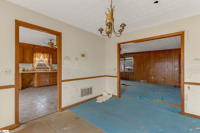 spare room with ceiling fan with notable chandelier, a textured ceiling, light tile floors, and wooden walls