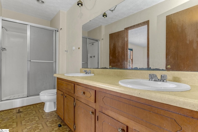 bathroom with oversized vanity, walk in shower, toilet, a textured ceiling, and double sink