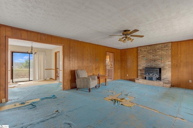 unfurnished living room featuring wood walls, light carpet, ceiling fan with notable chandelier, a brick fireplace, and brick wall