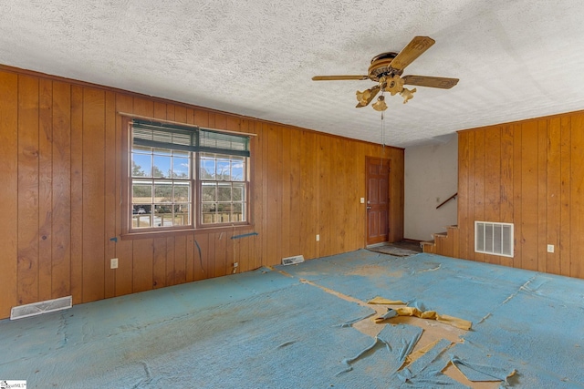 carpeted spare room featuring wood walls, ceiling fan, and a textured ceiling