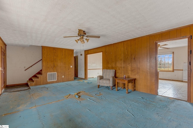 interior space with a textured ceiling, ceiling fan, and wooden walls