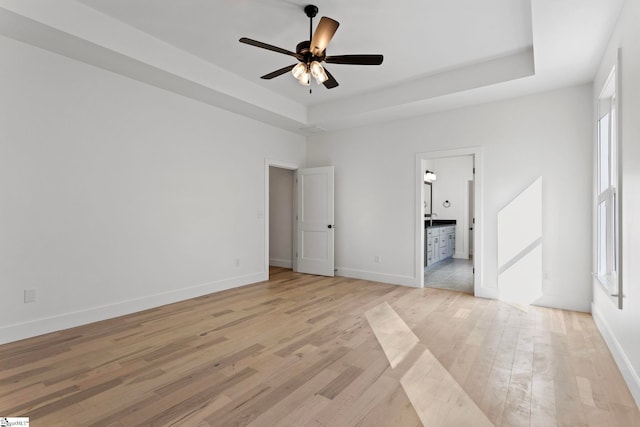 unfurnished bedroom with connected bathroom, a raised ceiling, ceiling fan, and light wood-type flooring