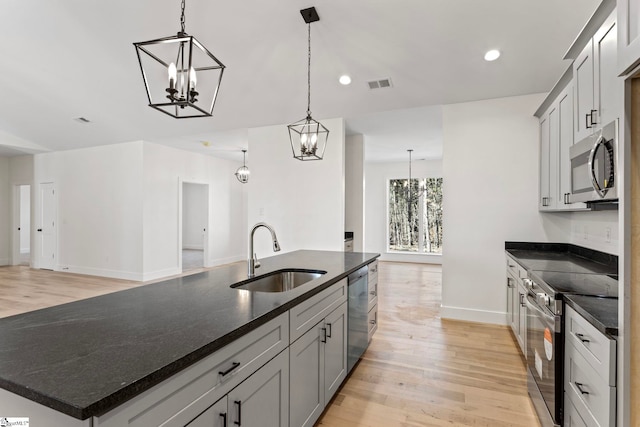 kitchen with appliances with stainless steel finishes, an island with sink, sink, hanging light fixtures, and an inviting chandelier