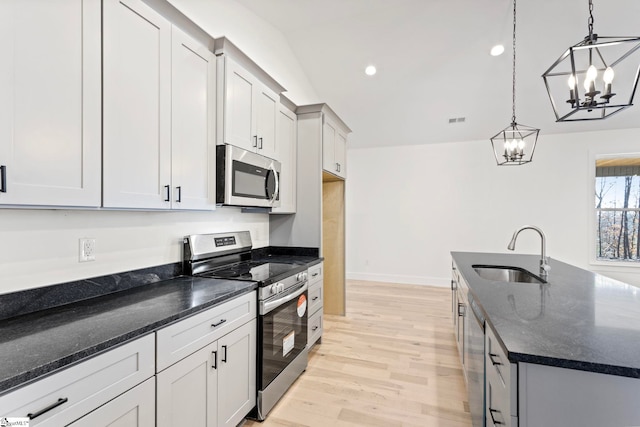 kitchen featuring sink, appliances with stainless steel finishes, dark stone countertops, an island with sink, and decorative light fixtures