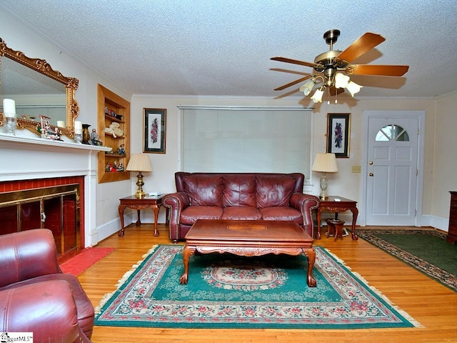 living room with light hardwood / wood-style flooring, ceiling fan, a fireplace, and a textured ceiling